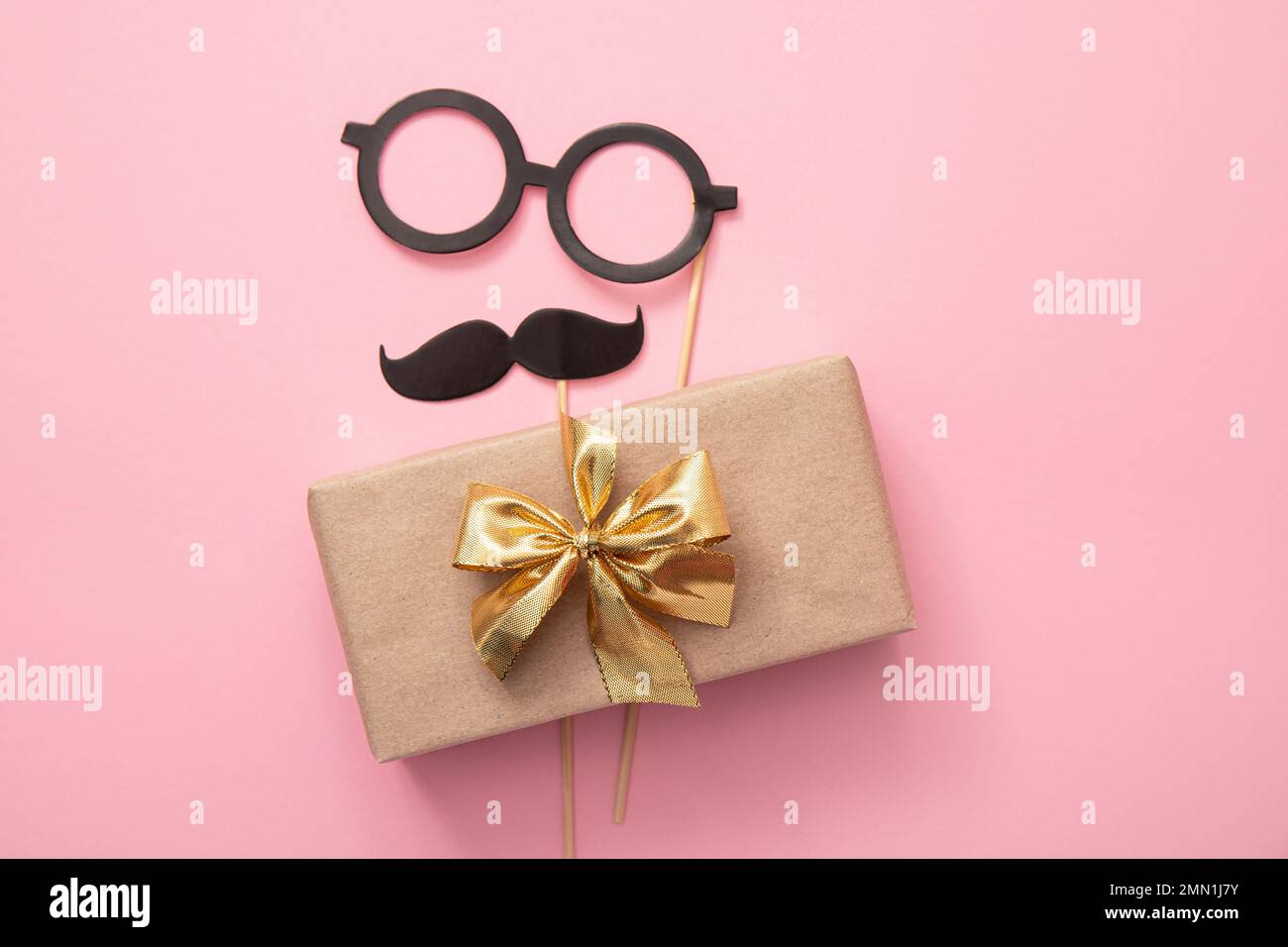 Flat lay view of packed Father`  s day present with mustache and glasses on pink background, lot of copy space. Fun greeting card mock up. Stock Photo